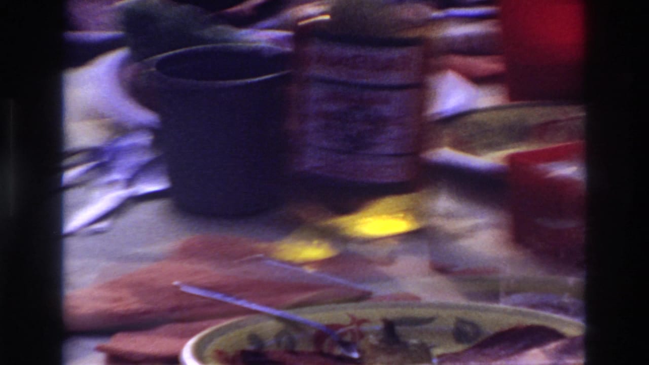 Table setting with blue mug, jar, red cup, plates, napkin, and blurred hands around food.