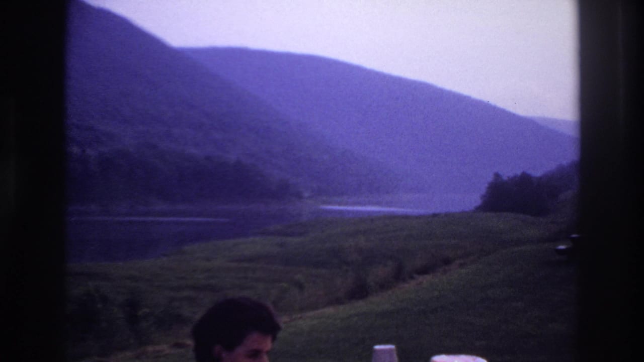 1967 Ottawa-area home-movie view of a narrow lake or river between green hills, with a partial dark-haired person low in frame.