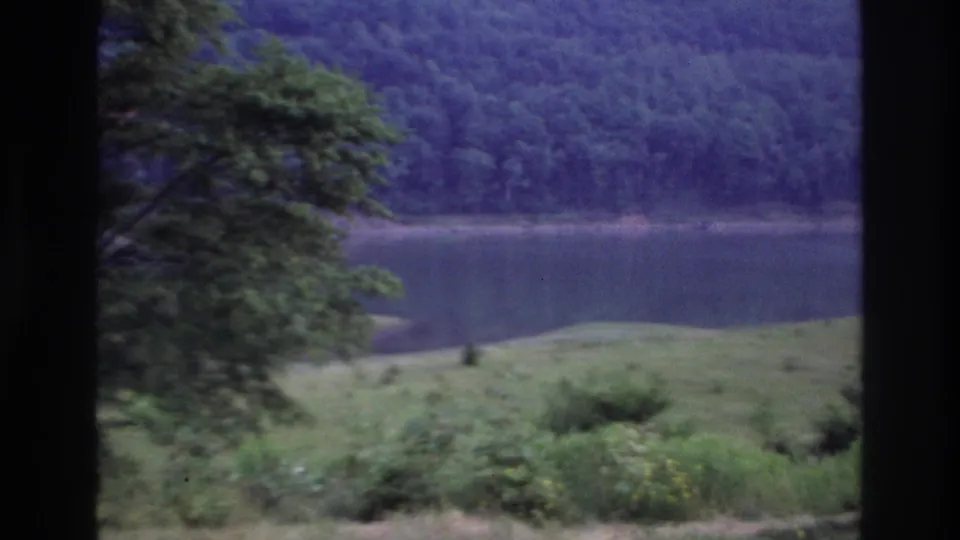 A lakeside landscape near Ottawa in 1967 appears with a foreground tree, grassy bank, still water, and wooded hillside.