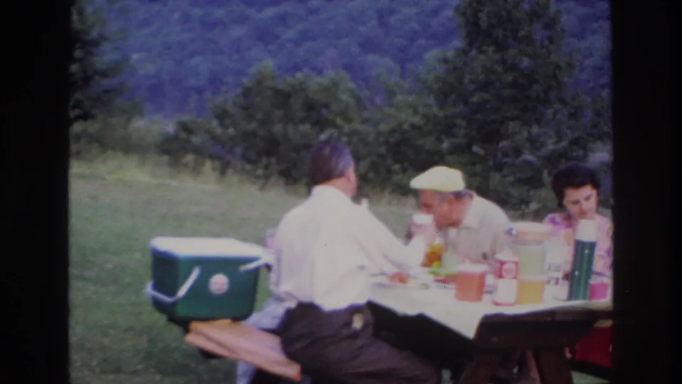 A 1967 Ottawa picnic scene shows three adults at a wooden table with a white cloth, green cooler, and drink items in a grassy setting.