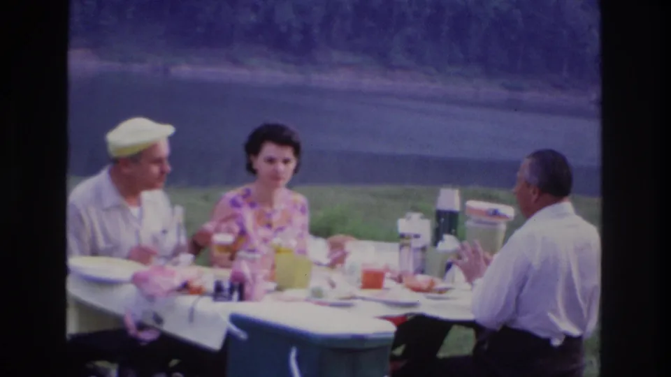 At the end of the clip, the woman faces the camera while two men remain seated at the 1967 Ottawa lakeside picnic table.