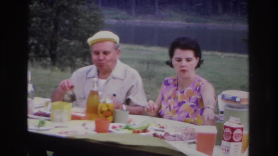 At the outdoor picnic in Ottawa, the seated couple face the camera as plates, cups, a bottle, and packaged milk sit on the table.