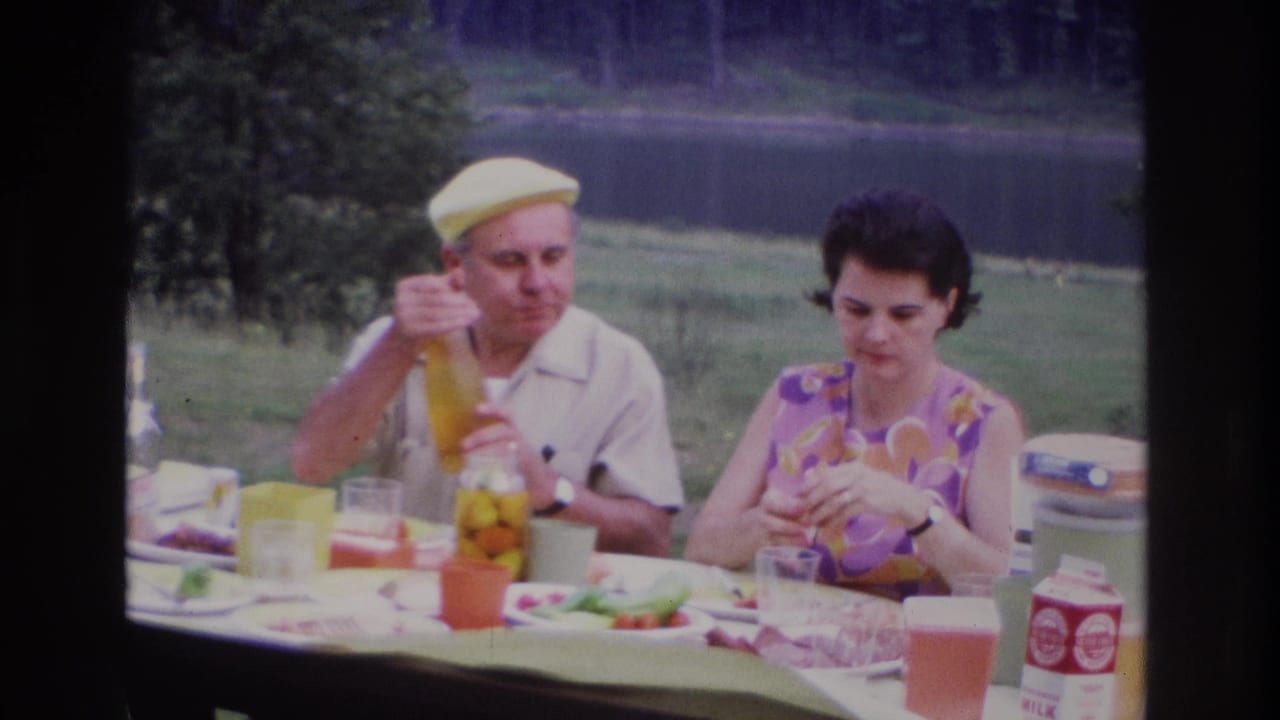 1967 Ottawa home-movie frame of a couple at an outdoor picnic table, with the man holding a bottle and the woman handling food.