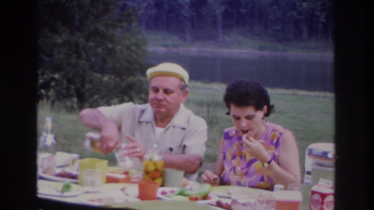 1967 Ottawa picnic scene showing a woman eating and a man pouring a drink at a table set with food beside a lake.