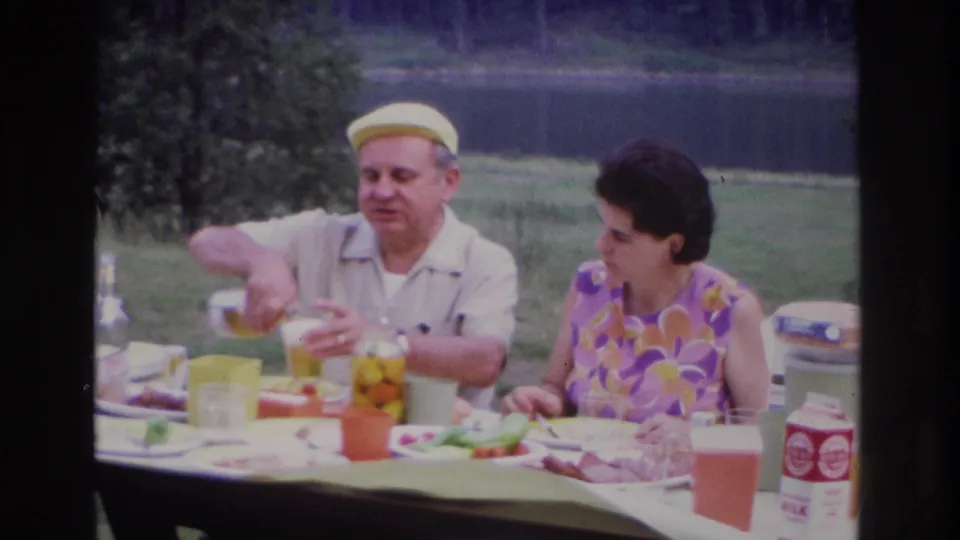 1967 Ottawa picnic frame showing a man pouring into a glass as a woman sits nearby with food and cartons on the table.