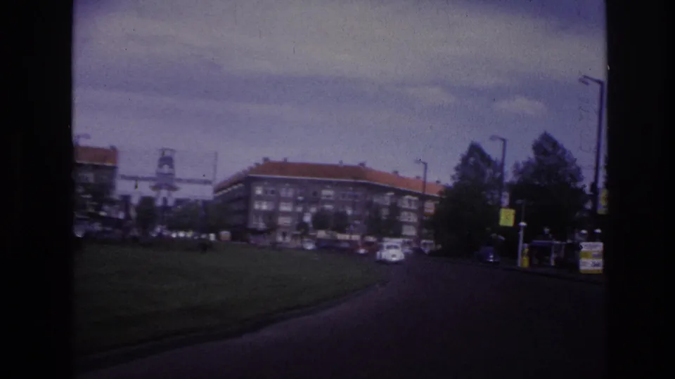 1967 Paris street scene from a moving vehicle, with apartment blocks, a grassy verge, parked cars, and trees.