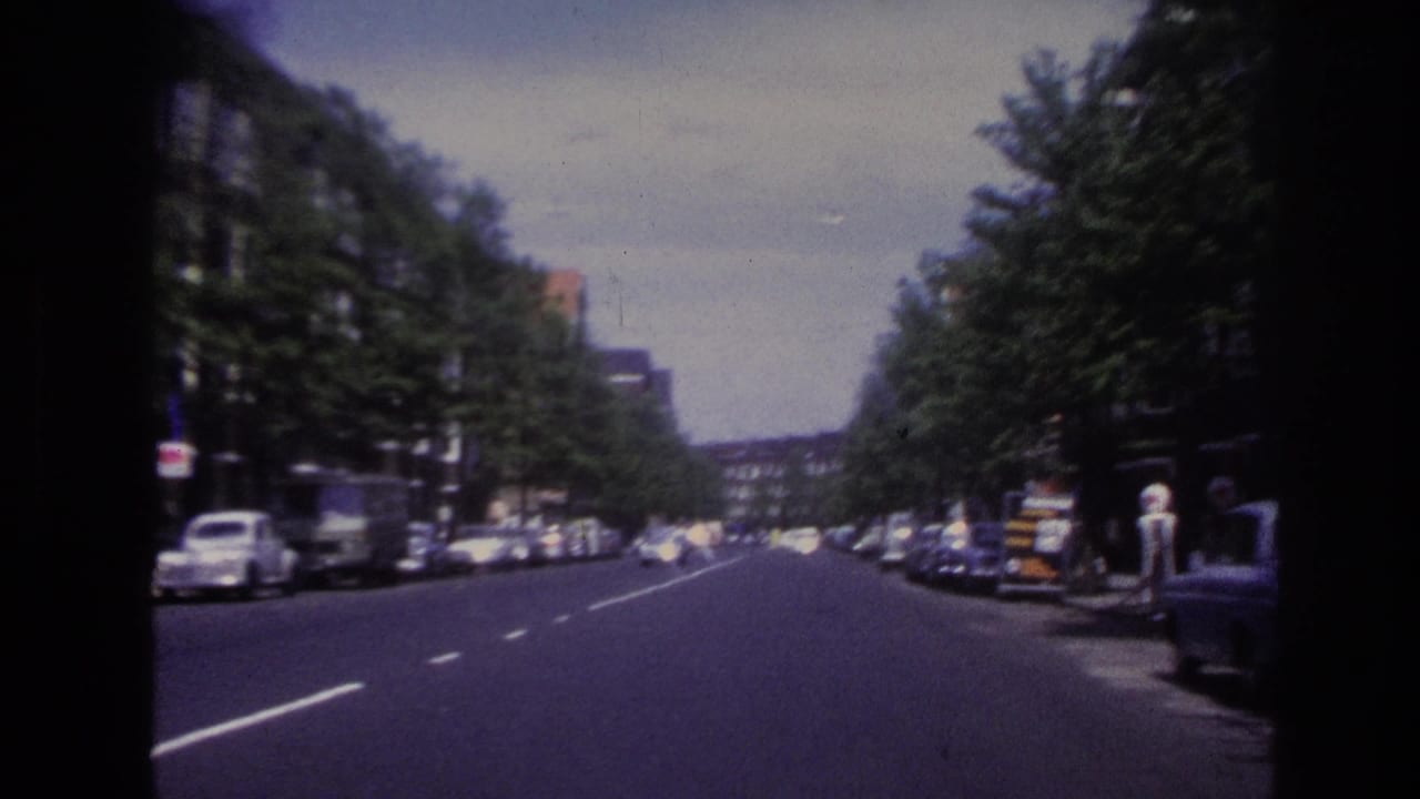 1967 Paris street view from a moving vehicle, showing a broad road, parked cars, trees, and apartment buildings.