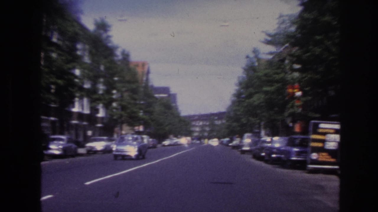 Moving view along a Paris street in 1967, with cars in the roadway, parked vehicles, trees, and building facades.