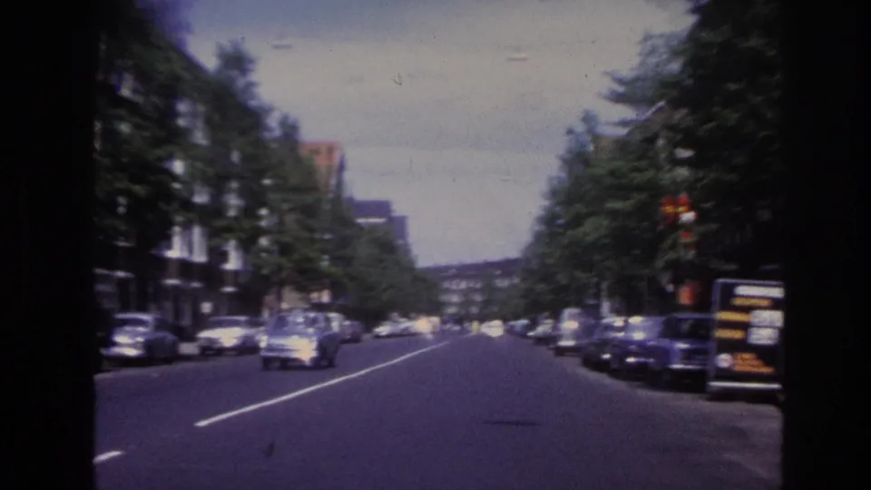 Moving view along a Paris street in 1967, with cars in the roadway, parked vehicles, trees, and building facades.