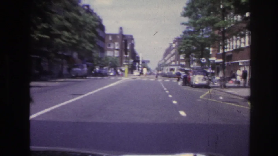 1967 Paris street view from inside a moving car, with apartment facades, roadside trees, parked vehicles, and pedestrians.