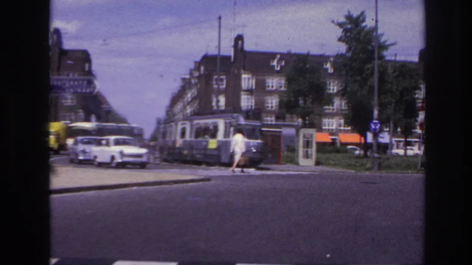 1967 Paris street view with a woman crossing near mid-century cars, a tram or streetcar, apartment blocks, and roadside signs.