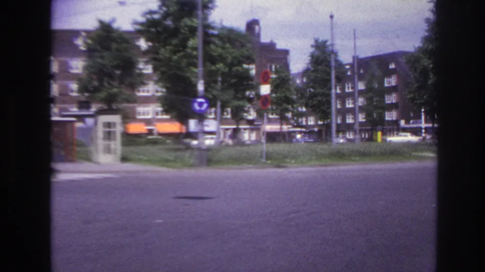 End of the 1967 Paris vehicle turn, with motion blur across a broad roadway, street signs, trees, apartment buildings, and distant cars.