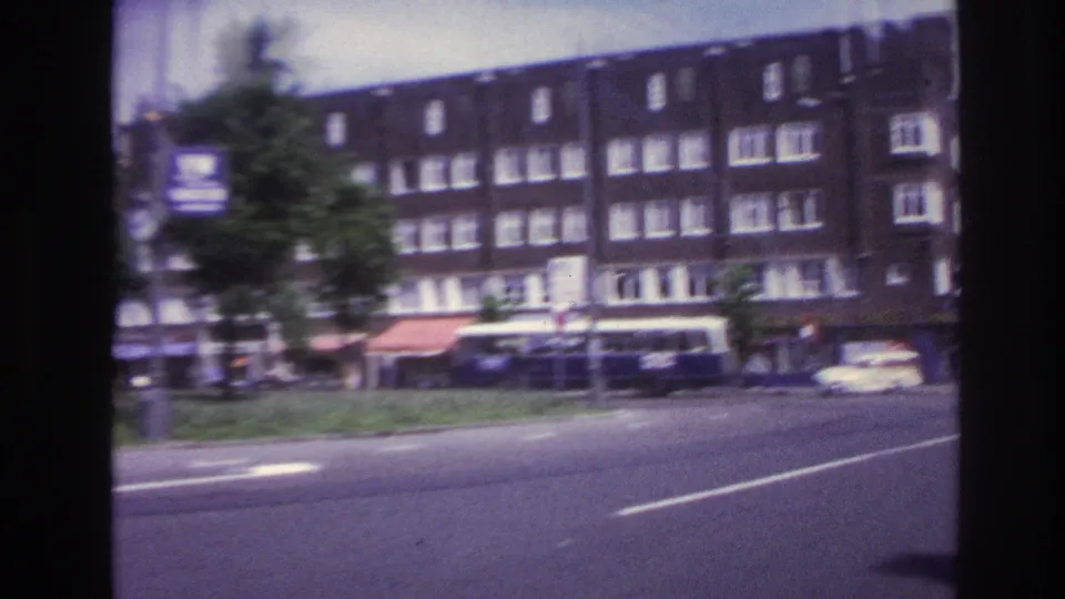 1967 Paris street view with large apartment buildings, shop awnings, street trees, and cars moving or parked along a broad road.