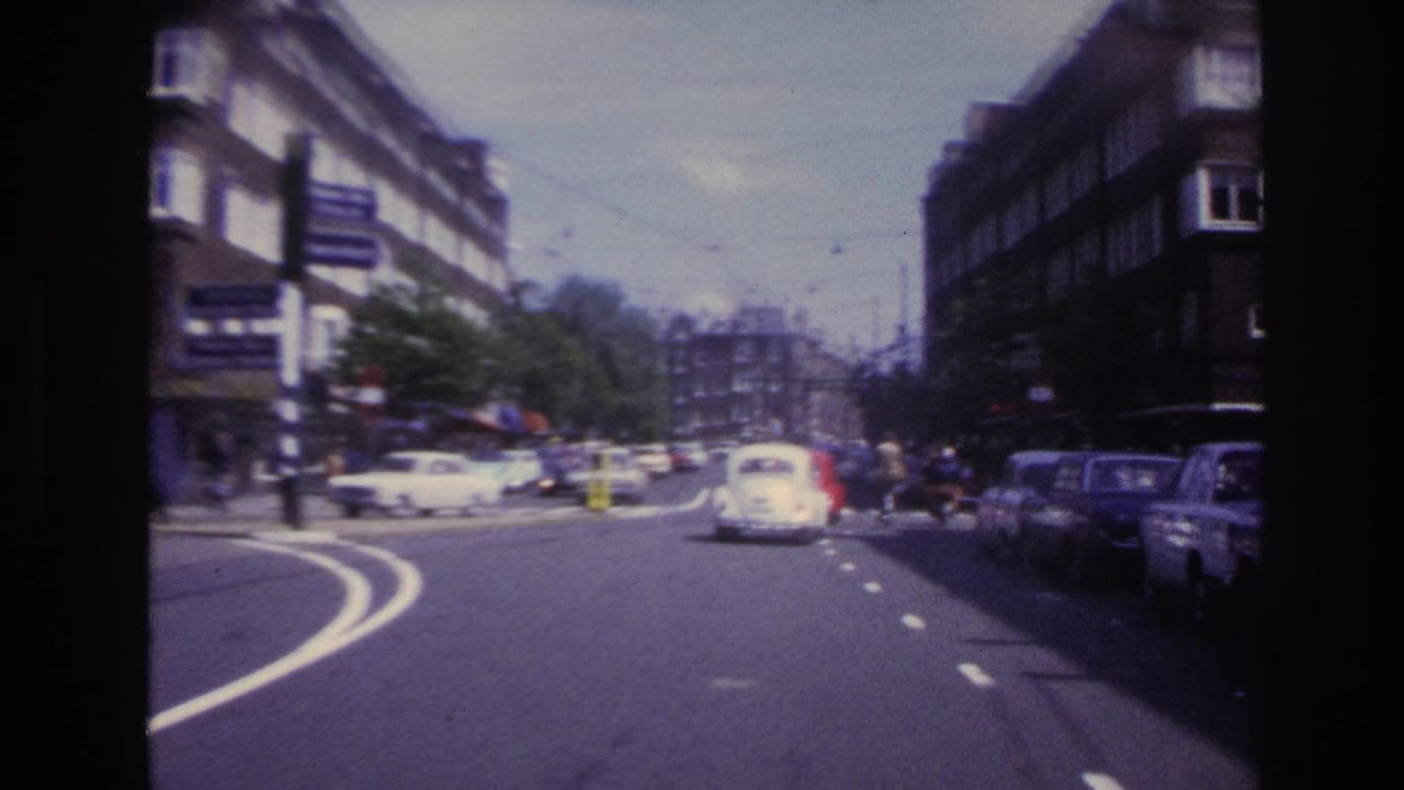 1967 Paris street view with classic cars, lane markings, apartment blocks, and soft 8mm motion blur from a moving viewpoint.