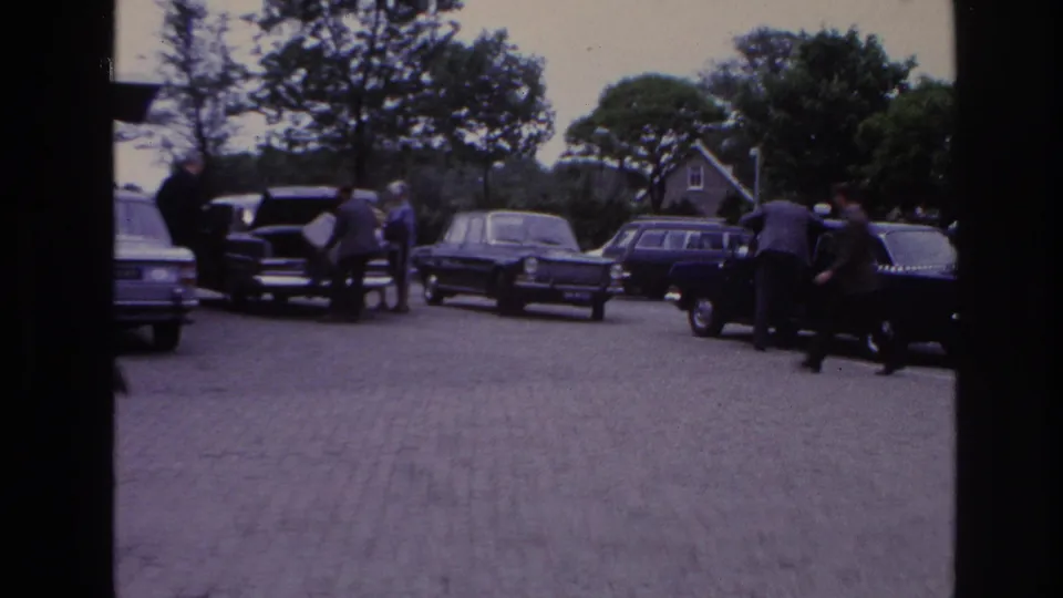1967 Paris parking scene with multiple classic cars, adults near open doors, trees, and a house-like building beyond the lot.