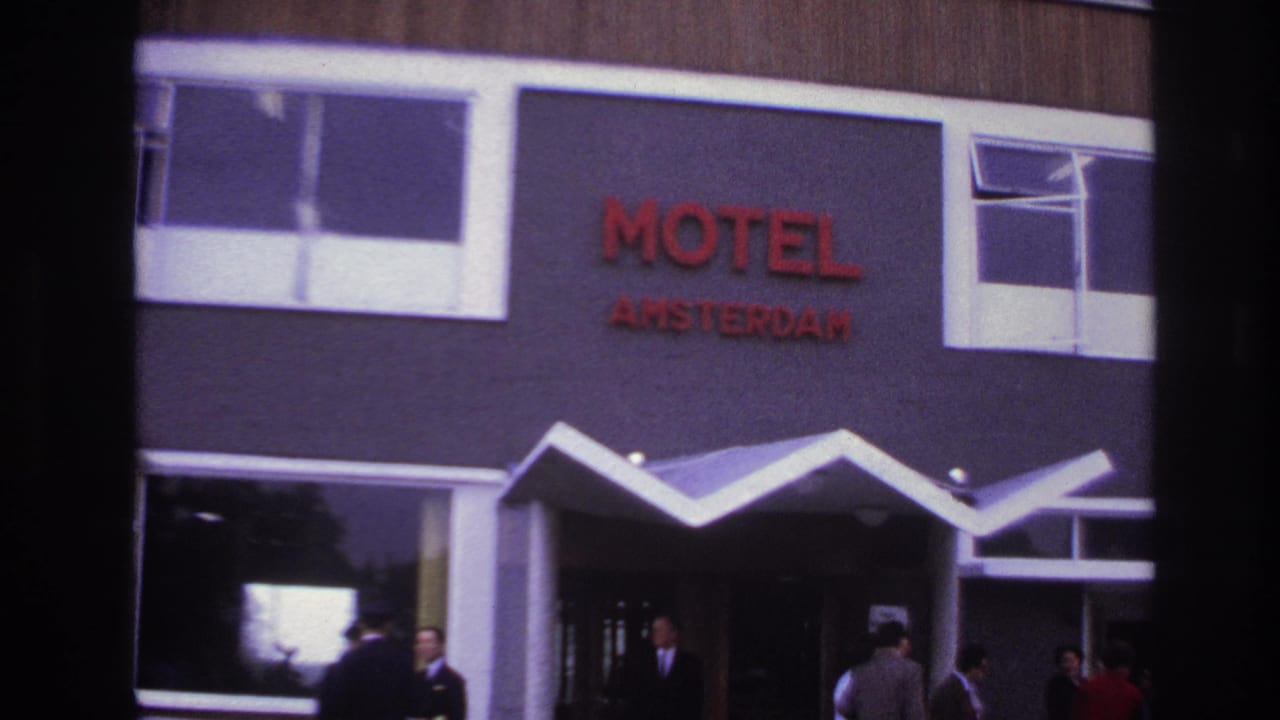 1967 Paris home-movie frame showing the Motel Amsterdam facade, red lettering, white zigzag awning, people near the entrance, and a light-colored car.
