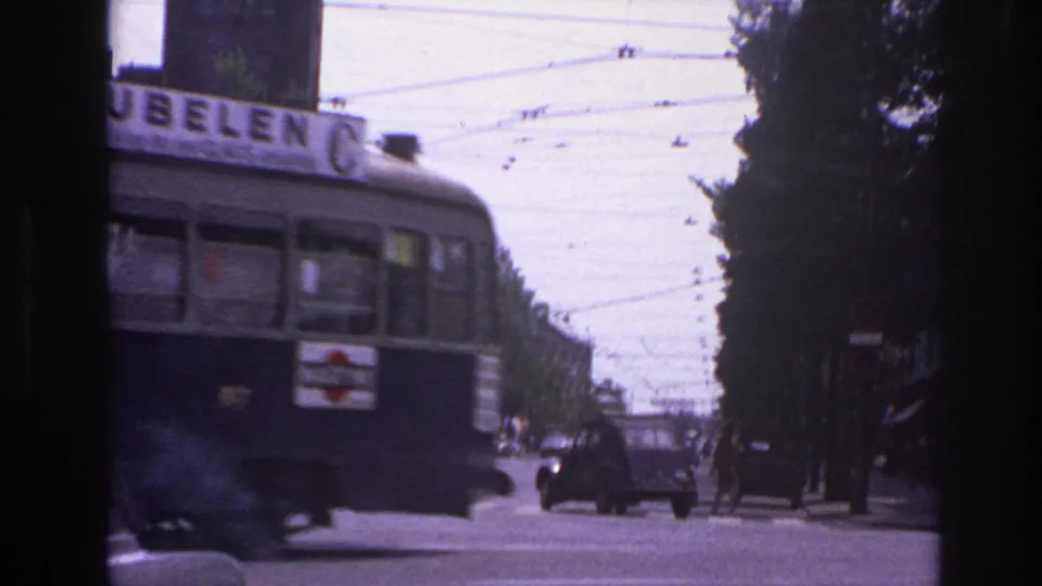 1967 Paris traffic scene with the rear of a trolley or bus, visible advertisement text, overhead cables, and cars in the distance.