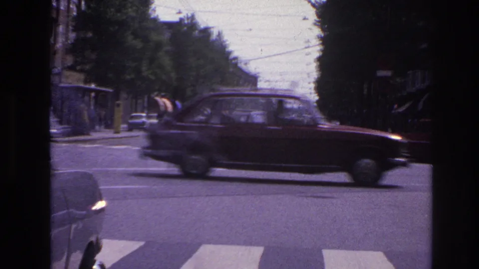 1967 Paris street frame showing a dark period car crossing a marked intersection beneath overhead transit wires.