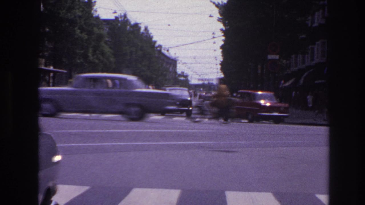 1967 Paris street traffic with classic cars crossing a broad intersection under overhead wires, viewed from inside a vehicle.
