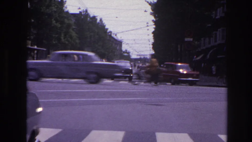1967 Paris street traffic with classic cars crossing a broad intersection under overhead wires, viewed from inside a vehicle.