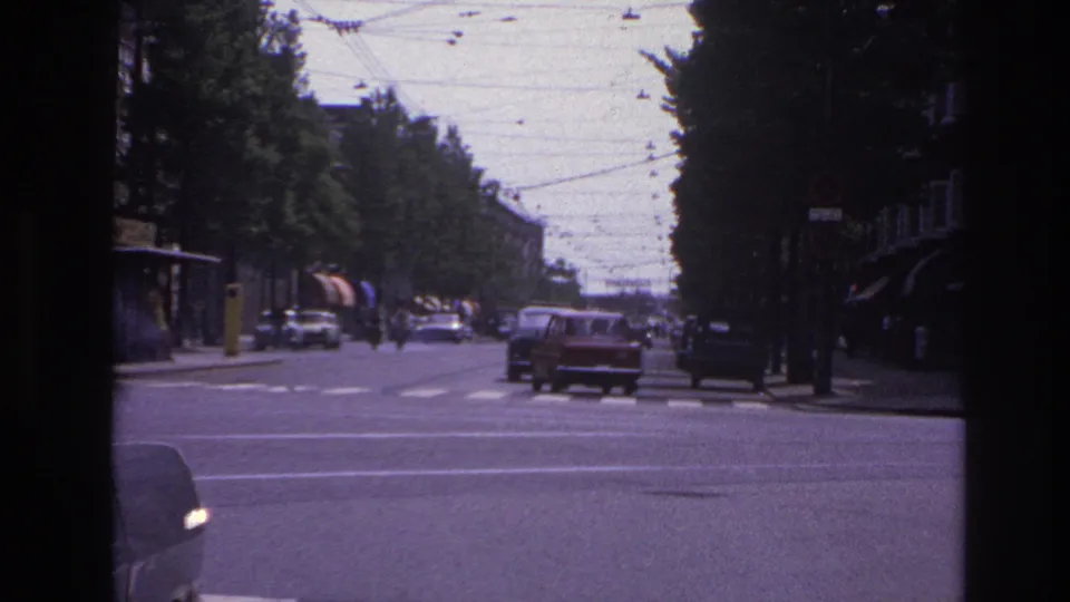 Classic cars travel along a broad Paris boulevard in 1967, with overhead wires, roadside trees, and dark window framing visible.