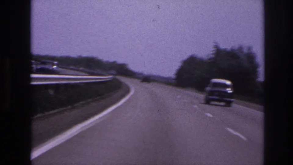 The later frame shows a classic car on a curving road, with roadside trees, guardrail, soft focus, and 8mm film grain.