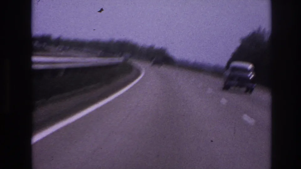 1967 Paris-area road scene with a classic car on a multi-lane highway, framed by guard rail, trees, and purple-tinted 8mm grain.