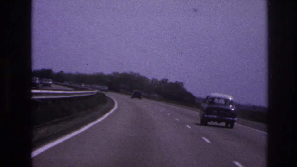 1967 Paris-area highway footage showing a car in the right lane, distant traffic, guard rails, trees, and visible 8mm film texture.