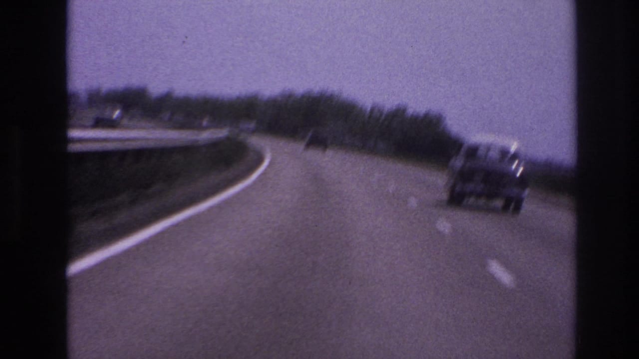 1967 8mm frame from Paris, France metadata showing a curved paved highway with a car ahead, roadside trees, and guardrail edges.