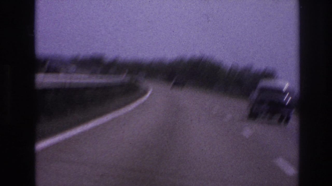 Car on a curving road, partly blurred, with guardrails and trees beside the highway.