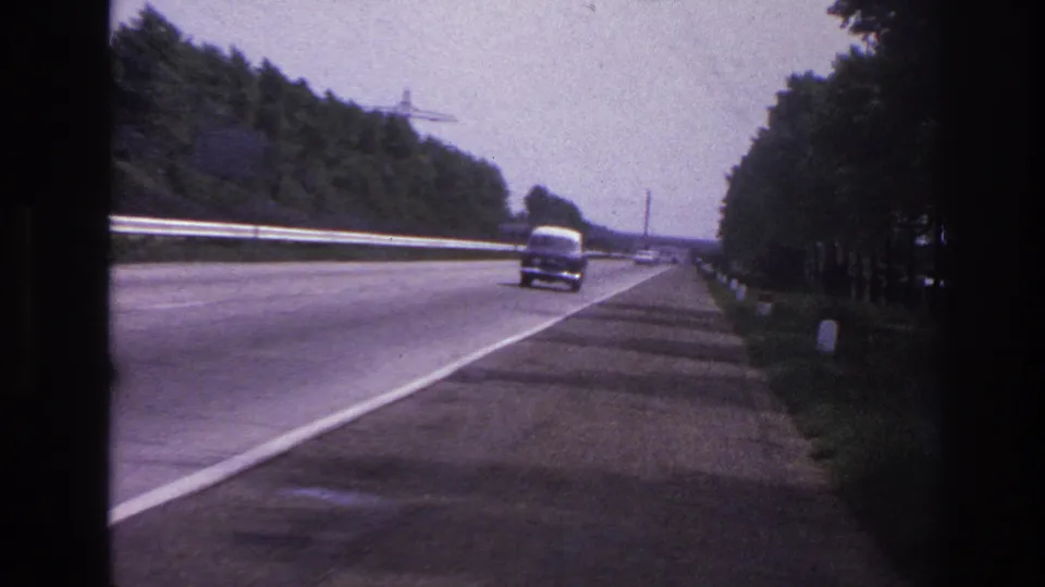 1967 8mm frame from the Paris, France clip showing a car farther down the highway, with trees, guardrails, and a roadside shoulder.