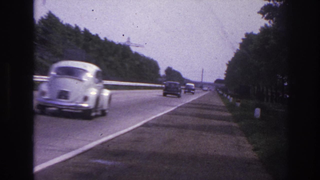 1967 Paris-area road footage with a white rounded compact car passing near the camera on a tree-lined highway.