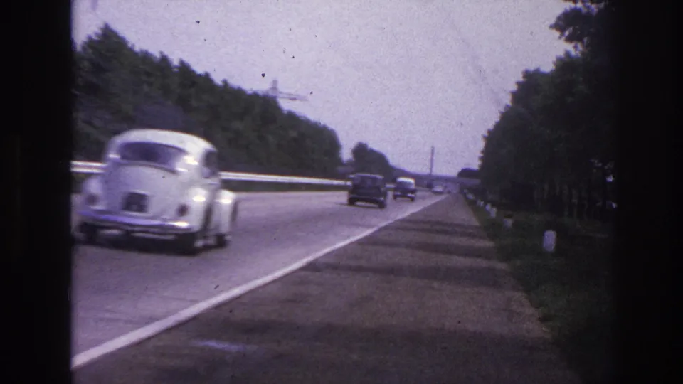 1967 Paris-area road footage with a white rounded compact car passing near the camera on a tree-lined highway.