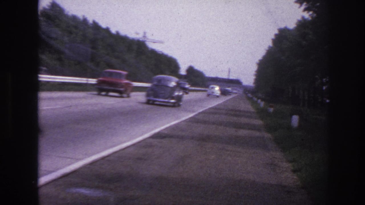 Divided roadway with vintage cars passing beside trees.