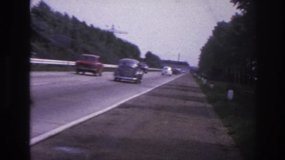 1967 Paris-area home-movie frame showing a roadway with period cars, trees, and soft 8mm color.