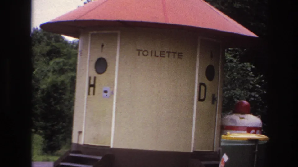 Closer 1967 France travel frame showing the octagonal TOILETTE structure, red roof, H and D markings, and surrounding greenery.
