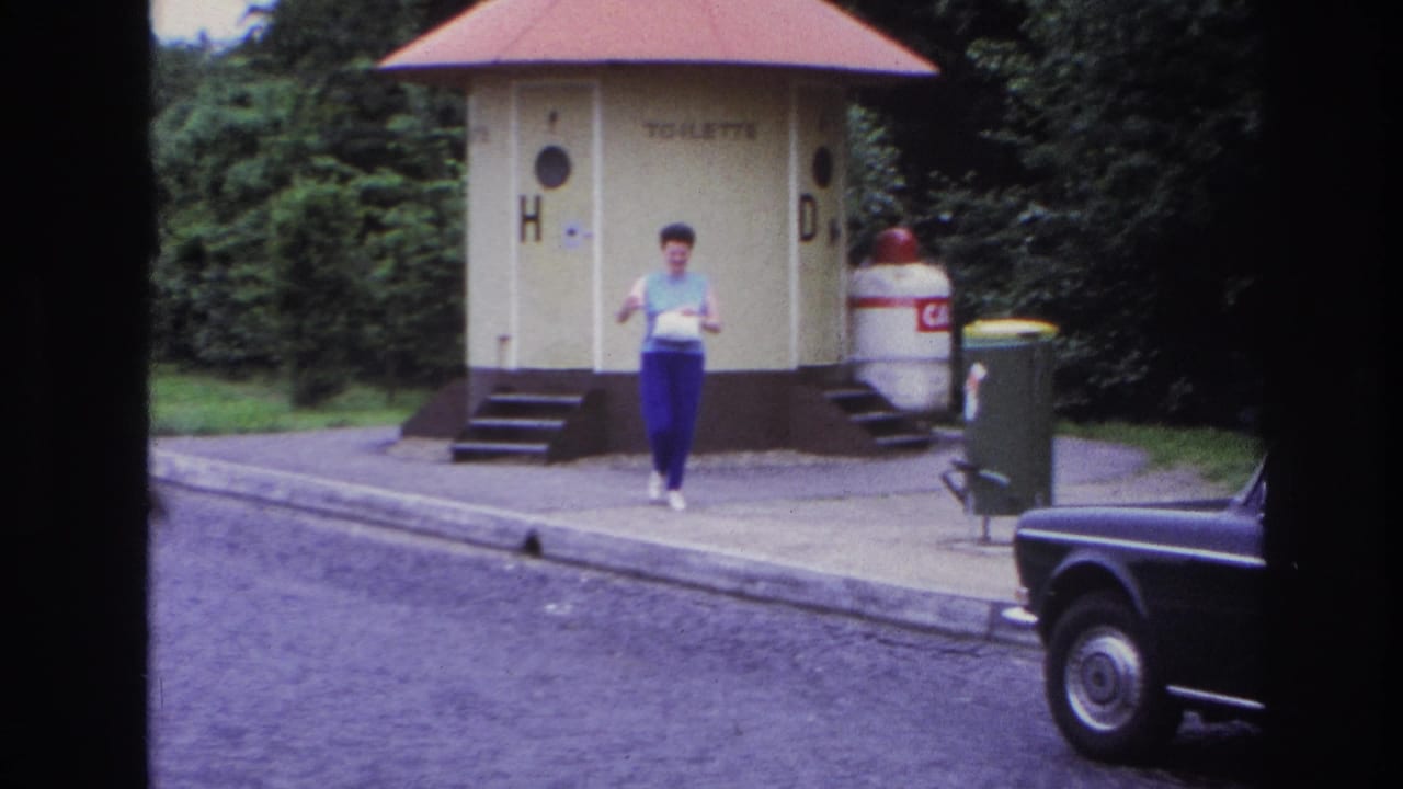 1967 Paris frame with a woman carrying a light bag near public toilet kiosks, trash bins, a curb, and a dark car at frame edge.