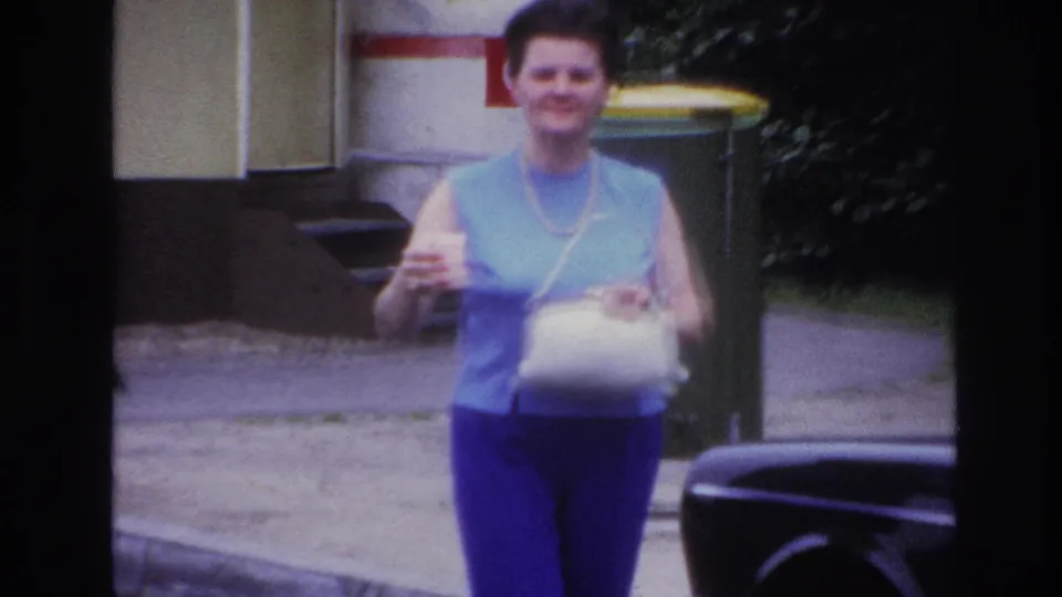 Near the end of the 1967 Paris clip, the woman is close to camera with a white bag and cup, framed by a sidewalk and bin.