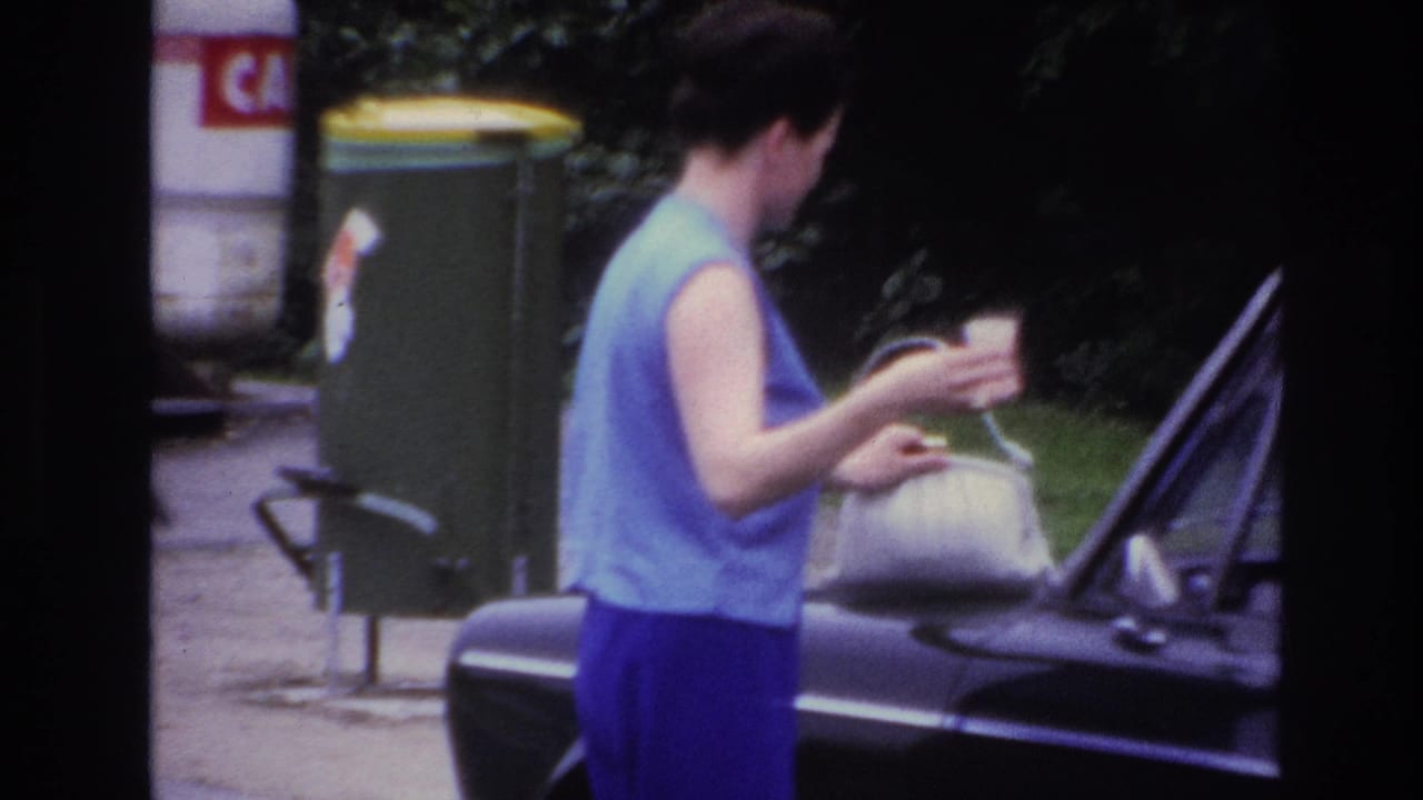 The woman stands at the side of a dark car in Paris, holding a cup while positioning her white handbag near the hood.