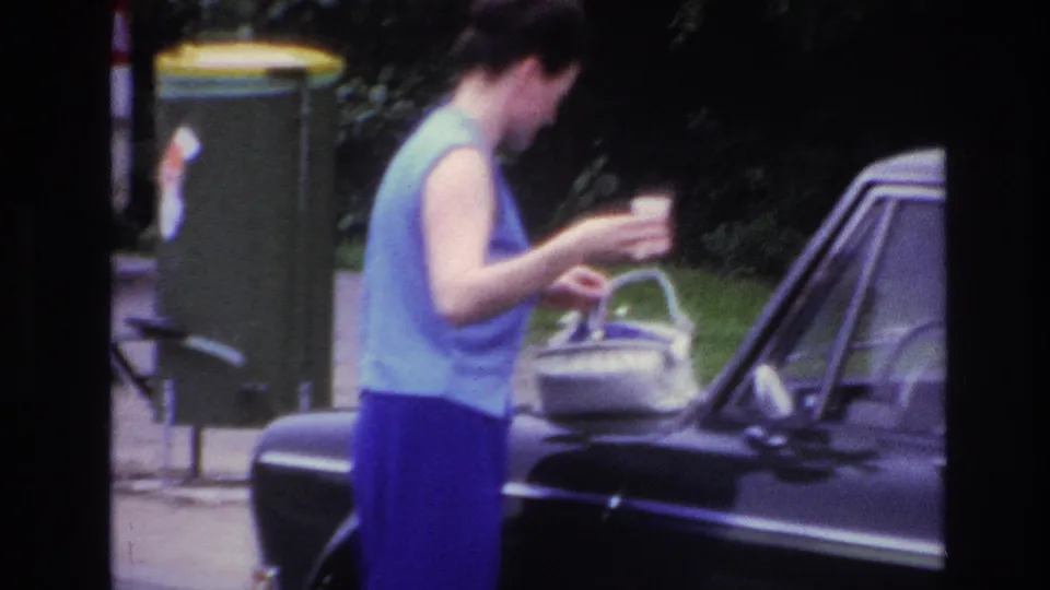 A side view shows the woman leaning toward the car, using the hood area for her handbag while keeping a small cup in hand.