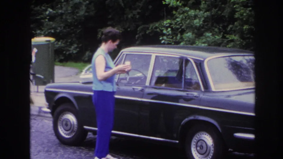 The woman remains beside the dark sedan on a Paris street, looking down as if preparing to open the door.