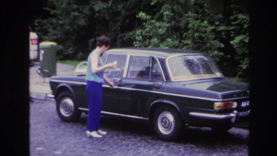 A wider frame shows the woman reaching for the dark sedan door handle on a cobblestone Paris street.