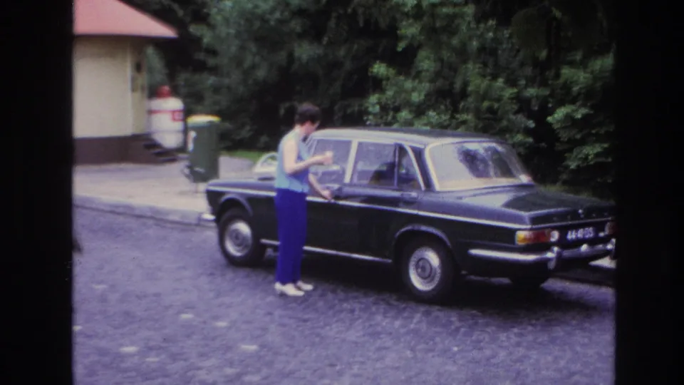 The closing frame shows the woman beside the dark sedan, with the rear of the car and street setting more visible.