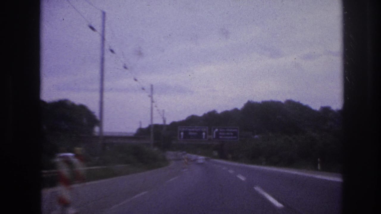Highway curve ahead with overhead direction signs and roadside trees under a cloudy sky.