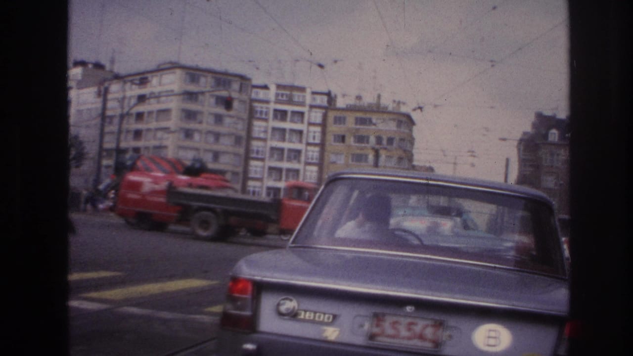 Grey BMW in foreground with driver, red cement mixer truck, and apartment blocks beyond.