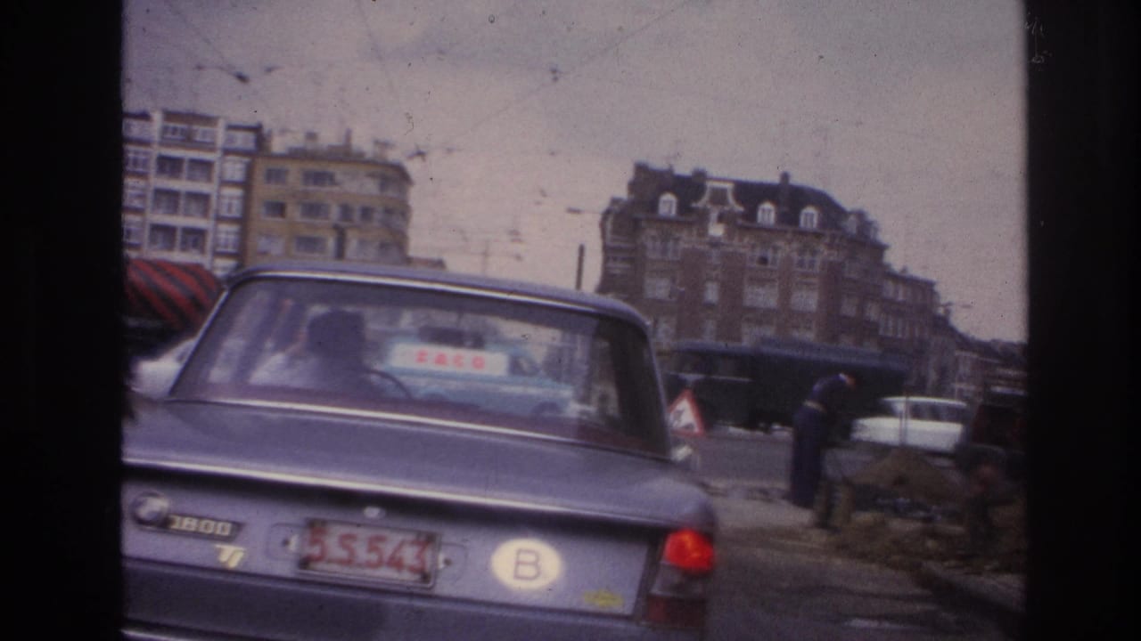 1967 Paris street view with a blue BMW in the foreground, workers near dirt piles, and apartment blocks beyond the road.