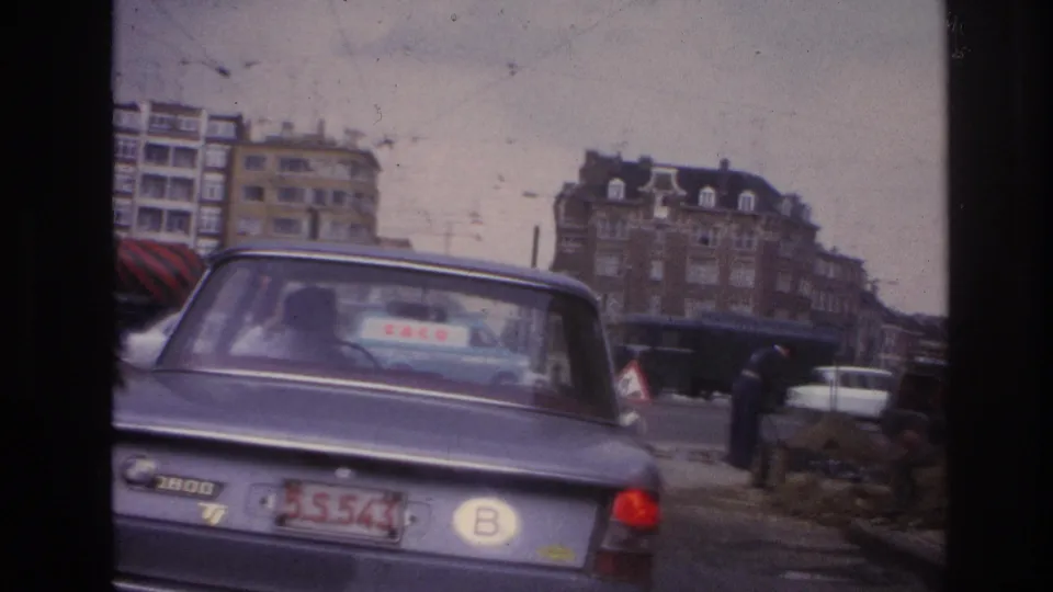 1967 Paris street view with a blue BMW in the foreground, workers near dirt piles, and apartment blocks beyond the road.