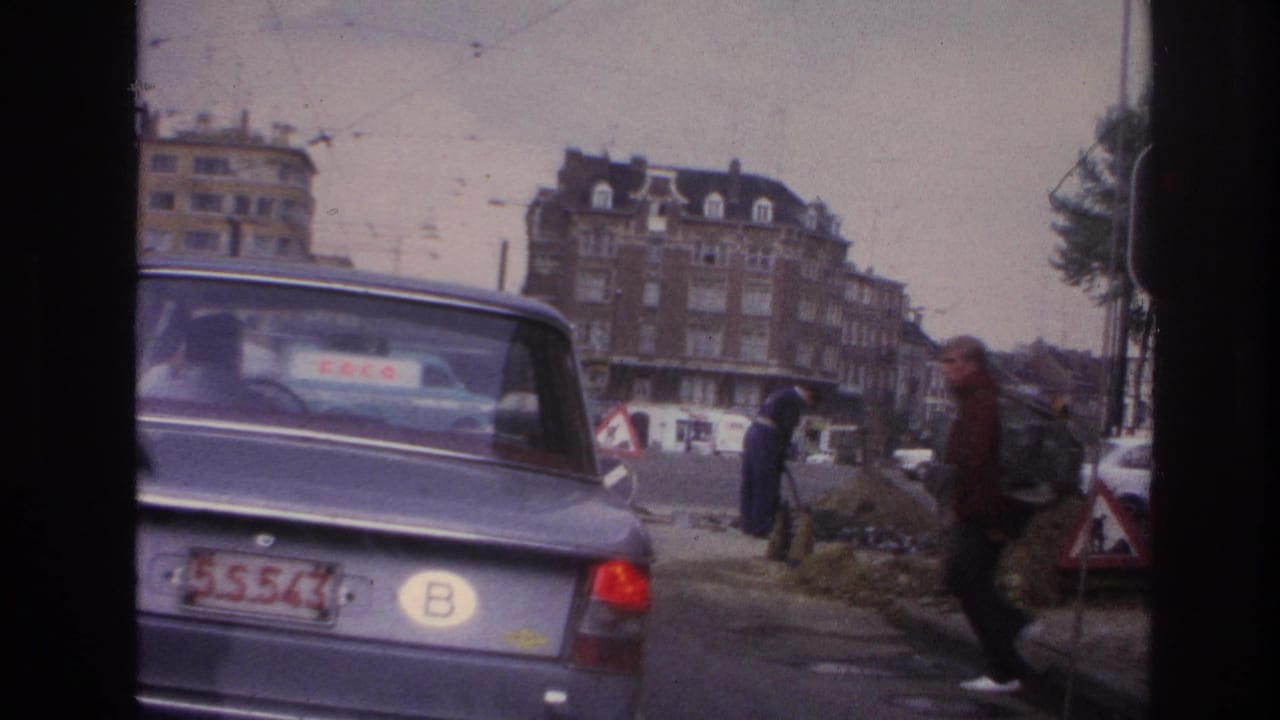 Paris street traffic in 1967, with the rear of a blue BMW, a pedestrian passing roadwork, and apartment buildings in the background.