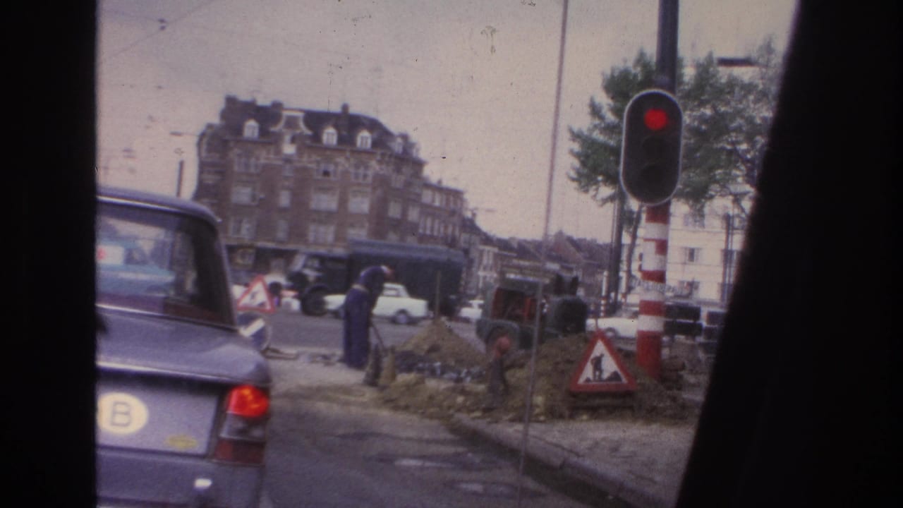 1967 Paris street view with classic cars, a red traffic signal, road work, pedestrians, and multi-story apartment facades.