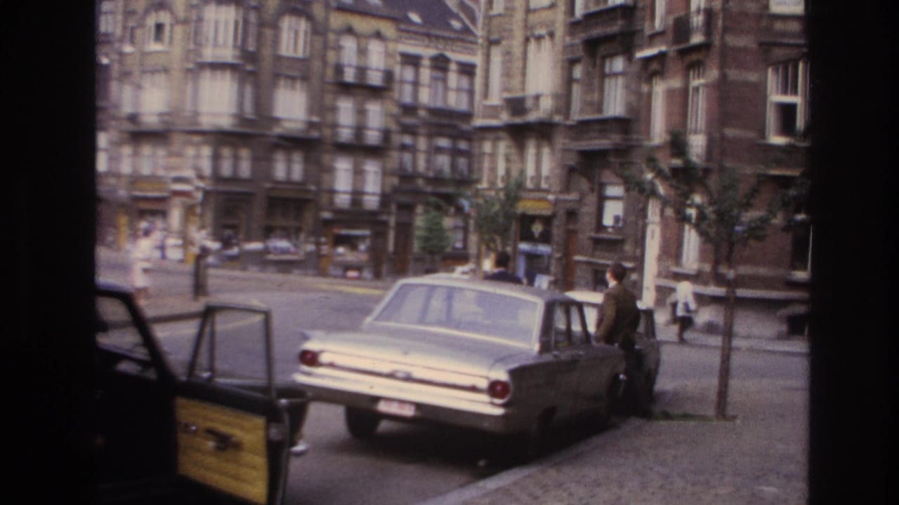 1967 Paris curbside view of a light-colored sedan, open car door, pedestrians, and older apartment facades across the street.